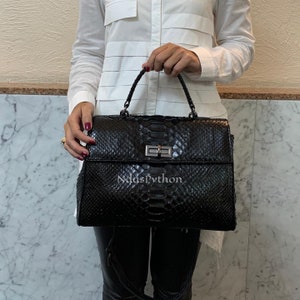 May include: Black leather handbag with a snakeskin pattern and a silver lock. The bag has a top handle and a detachable shoulder strap.