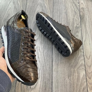 Pode incluir: Um par de tênis de couro marrom com padrão de pele de cobra. Os tênis têm uma sola branca e um fecho de cadarço preto.