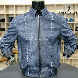 以下が含まれることがあります： ジッパー留めと白いステッチが付いた青いパイソンレザーのボンバージャケット。ジャケットは襟と長袖です。