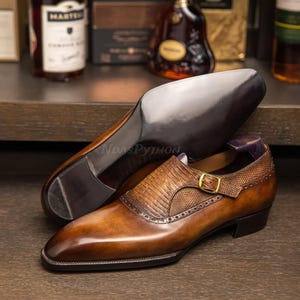 May include: Brown leather dress shoes with a buckle strap and a textured pattern on the toe. The shoes have a pointed toe and a low heel.