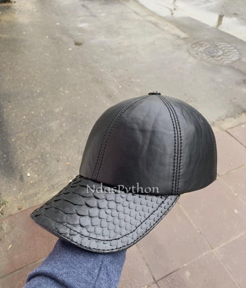 May include: A black leather baseball cap with a snakeskin patterned brim. The cap has a stitched seam down the center of the crown.