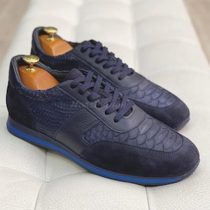 Puede incluir: Un par de zapatillas de cuero azul marino con estampado de piel de serpiente. Las zapatillas tienen una suela de goma azul.