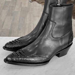 Puede incluir: Un par de botines de cuero negro con punta y empeine texturizado. Las botas tienen cierre de cremallera y tacón apilado. Las botas miden aproximadamente 15 cm de altura.