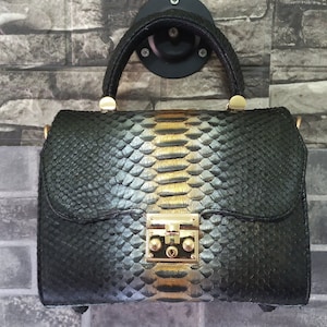 May include: A black handbag with a gold clasp and a snakeskin pattern. The bag is hanging on a hook.