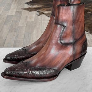 Op de afbeelding: Een paar bruine leren enkellaarsjes met een puntige neus en een getextureerde, donkerbruine wreef. De laarzen hebben een zijrits en een blokhak. Het leer heeft een gepolijste afwerking.