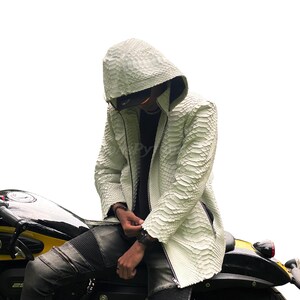 May include: White textured hooded jacket with a zip. The jacket is worn with black jeans and a black motorcycle. The jacket's texture resembles snakeskin.
