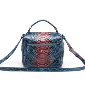 May include: A boxy handbag with a top handle and a detachable shoulder strap. The bag is crafted from snakeskin in shades of blue, red, and black. It features a zip closure and the text "NdasPython".