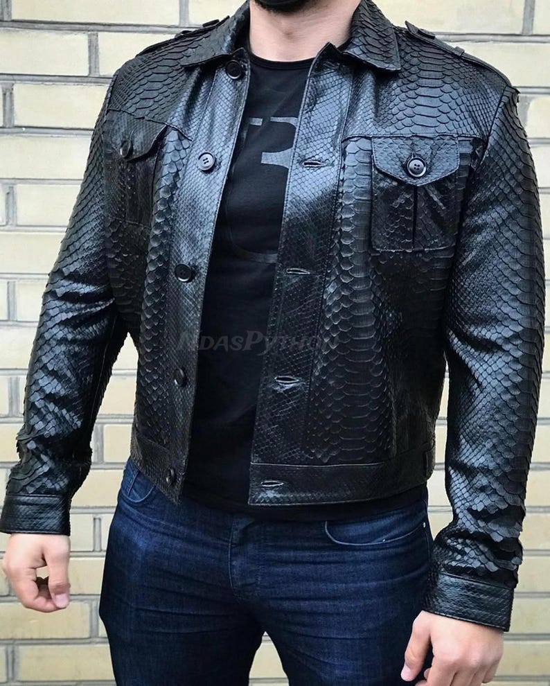 Pode incluir: Casaco de couro preto com padr&atilde;o de pele de cobra, com fecho de bot&otilde;es, dois bolsos no peito e gola. O casaco &eacute; usado sobre uma camiseta preta e combinado com jeans azuis.