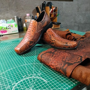 May include: Two brown leather shoes with a snakeskin pattern. The shoes are on a green cutting mat with a white protractor.