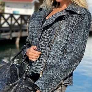 May include: A blue snakeskin leather jacket with a zipper closure and a gold zipper pull. The jacket has a stand-up collar and a zippered pocket on the left side.