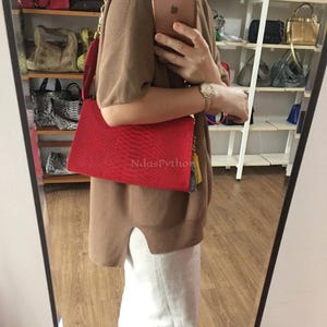 May include: A vibrant red rectangular handbag with a textured pattern. The bag has a gold chain strap and a tassel. The text "NdasPython" is visible on the bag. The bag is approximately 12 inches wide.