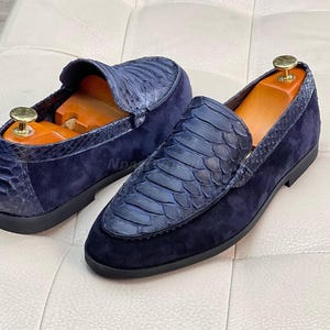 May include: A pair of blue suede loafers with a snakeskin pattern. The loafers have a pointed toe and a slip-on design.