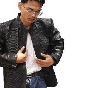 Peut inclure: Veste en cuir noire avec un motif peau de serpent. La veste a un col montant et une fermeture éclair. La personne porte un t-shirt blanc et un jean bleu. Un vêtement d'extérieur élégant.