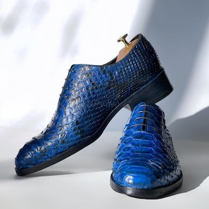 Może przedstawiać: Para niebieskich skórzanych butów ze wzorem skóry węża. Buty mają sznurowanie i spiczasty nosek.