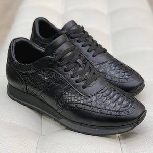 Könnte beinhalten: Schwarze Lederschuhe mit Schlangenhautmuster und weißer Gummisohle.