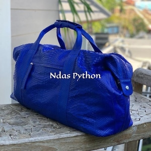 May include: A bright blue duffel bag with a snakeskin texture. The bag features two handles, a zip closure, and a small zipped pocket. The text "Ndas Python" is visible on the front of the bag.