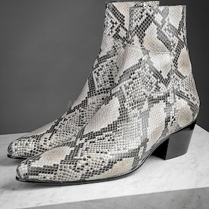 Puede incluir: Un par de botines de tobillo de piel de serpiente en blanco y negro con punta puntiaguda y tacón de bloque.