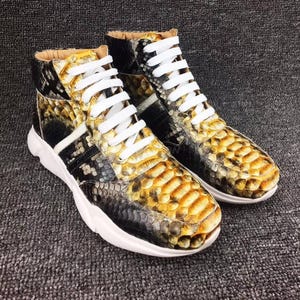 Puede incluir: Un par de zapatillas de deporte de caña alta con suela blanca y estampado de piel de serpiente negra y amarilla.