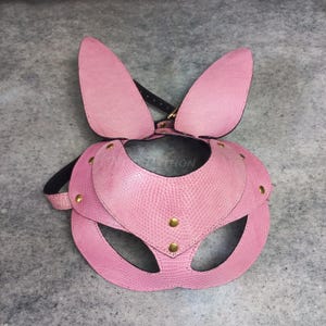 Peut inclure: Masque de lapin en cuir rose avec de longues oreilles, des découpes pour les yeux et une sangle de cou. Le masque a une surface texturée et est orné de rivets dorés. La conception comprend un collier et des sangles réglables.