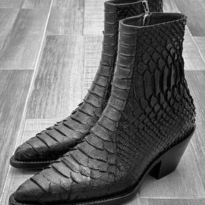 May include: A pair of black leather cowboy boots with a snakeskin pattern. The boots have a pointed toe and a block heel.