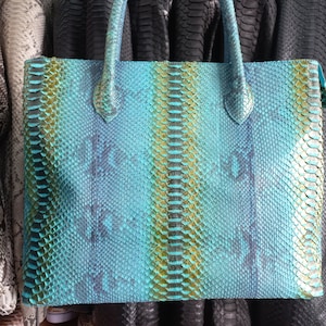 May include: A turquoise, green, and gold snakeskin tote bag with a structured shape and top handles.