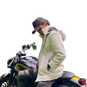 May include: A white, textured leather jacket with a hood and zip closure. The jacket is worn over a black and yellow motorcycle. The person is wearing a black baseball cap and grey jeans.