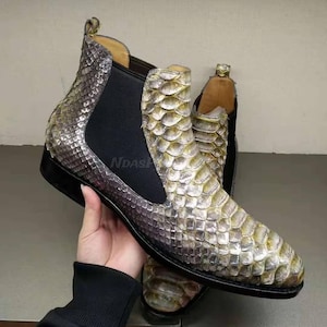 May include: A pair of ankle boots with a snakeskin pattern. The boots are a light brown colour with a black elastic panel on the back. The boots have a pointed toe and a low heel.