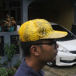 May include: A yellow snakeskin baseball cap with a curved brim. The cap is made of real snakeskin and has a unique texture.