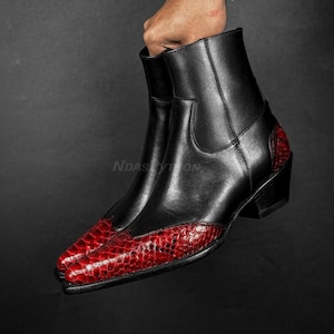 Puede incluir: Botas de tobillo de cuero negro con punta puntiaguda y un patrón de piel de serpiente roja en la parte delantera. Las botas tienen un tacón bajo.