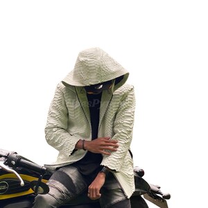 May include: A white, textured leather jacket with a hood, worn with distressed grey jeans. The jacket has a scale-like pattern and is worn over a black shirt. The person is seated on a black and yellow motorcycle.
