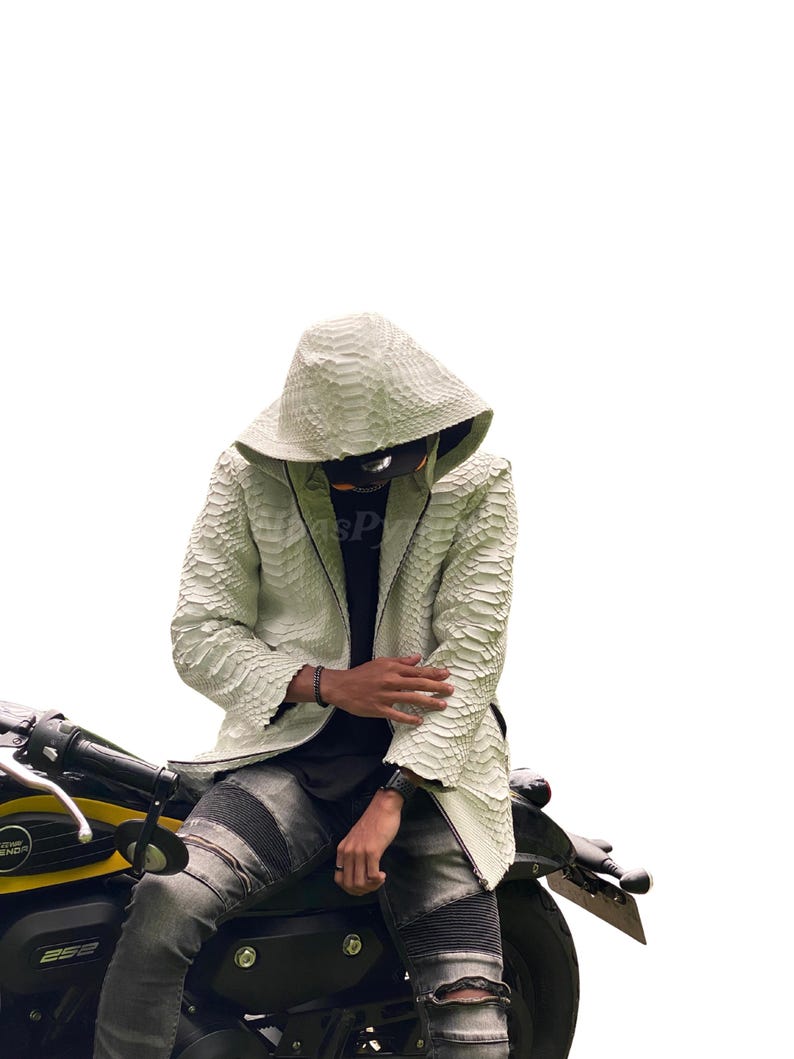 May include: A white, textured leather jacket with a hood, worn with distressed grey jeans. The jacket has a scale-like pattern and is worn over a black shirt. The person is seated on a black and yellow motorcycle.
