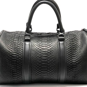 May include: A black leather duffel bag with a snakeskin pattern. The bag has two top handles and a zipper closure.