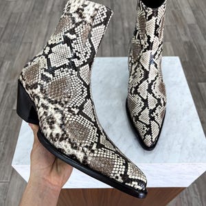 May include: A pair of black and white snakeskin cowboy boots with pointed toes and a zip on the back of the boot.