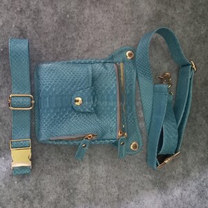 May include: A teal-colored, faux snakeskin fanny pack with a matching adjustable belt and shoulder strap. The bag features gold-toned zippers, buckles, and hardware. The fanny pack has a flap closure with a gold snap and a zippered pocket.
