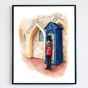Puede incluir: Una pintura de acuarela de un guardia británico de pie frente a una cabina telefónica azul. El guardia lleva un uniforme rojo y un gorro de piel de oso negro. La cabina telefónica está decorada con el escudo real.