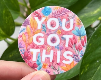 May include: A round sticker with a pink background and a floral pattern. The sticker says "You Got This" in white letters.