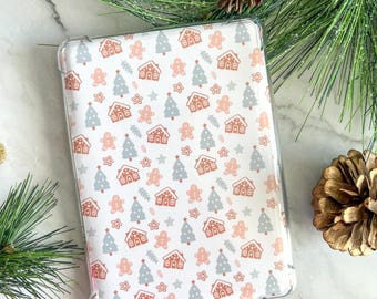 May include: Clear protective case featuring a repeating pattern of gingerbread houses, Christmas trees, and stars in shades of pink, gray, and brown. The case is designed for a tablet or e-reader, perfect for the holiday season.
