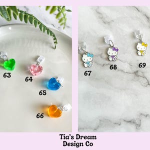May include: A collection of charms featuring hearts and Hello Kitty characters. The charms are made of clear plastic and have different colors, including green, pink, blue, and orange. The charms are numbered 62 through 70.
