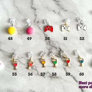 May include: A collection of 61 colorful charms, including a green frog, yellow macaron, pink macaron, red video game controller, white video game controller, rainbow, wine glass, avocado, and more. The charms are attached to clear plastic clips.