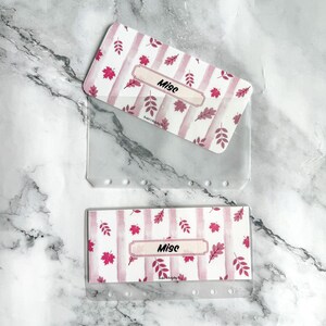 May include: Two rectangular clear plastic cash envelopes for binders, featuring a white and light pink vertical striped pattern with scattered pink autumn leaves. Each envelope has a central label area with the printed text Misc in black ink.