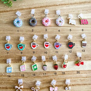 May include: Twenty-four different charm designs for a zipper pull or bag charm. The charms include donuts, coffee mugs, books, strawberries, cherries, and bows. The charms are all gold-colored with colorful enamel details.