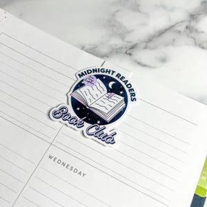 Puede incluir: Una pegatina azul y blanca con un libro, una luna creciente y estrellas. El texto dice "Midnight Readers Book Club" y "One more chapter".