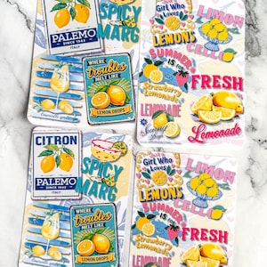 May include: Four rectangular sticker sheets featuring vibrant lemon-themed graphics. Designs include vintage-style signs for Citron Palermo, Spicy Marg, and Lemon Drops, alongside text-based illustrations reading Girl Who Loves Lemons and Lemonade.