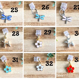 May include: A set of 10 charm pendants for keychains or jewelry making. The charms include a butterfly, a flower with a smiley face, and a balloon animal. The charms are numbered 25 through 33.