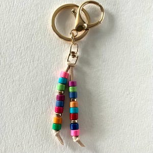 May include: A gold key chain with a colourful beaded tassel. The beads are in shades of pink, blue, green, orange, and yellow.