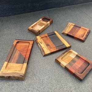 Puede incluir: Cinco bandejas de madera con diferentes patrones y colores de veta de madera. Las bandejas están hechas de varios tipos de madera, incluyendo nogal, arce y cerezo. Las bandejas son de diferentes tamaños y formas, y todas están hechas a mano.