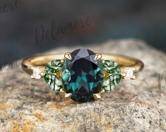 May include: A gold ring with a large, dark green gemstone surrounded by smaller green gemstones and two small white gemstones. The ring is set on a rough, gray rock.