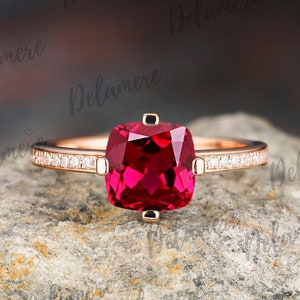 May include: A rose gold ring with a cushion-cut ruby gemstone surrounded by a row of small diamonds.