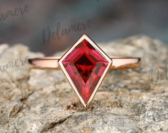 May include: A rose gold ring with a red, square-shaped gemstone set in a diamond-shaped setting.