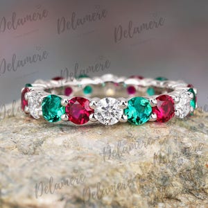 May include: A silver band ring with alternating emerald green, ruby red, and clear round gemstones.